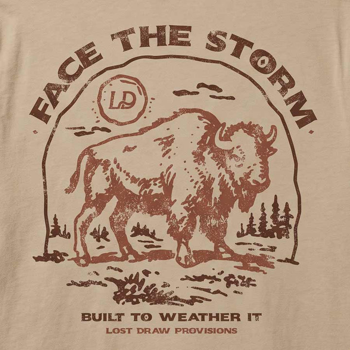 Close-up of a beige fabric surface with a distressed brown graphic print featuring a bison, the words “FACE THE STORM,” and smaller text reading “BUILT TO WEATHER IT” and “LOST DRAW PROVISIONS.”.