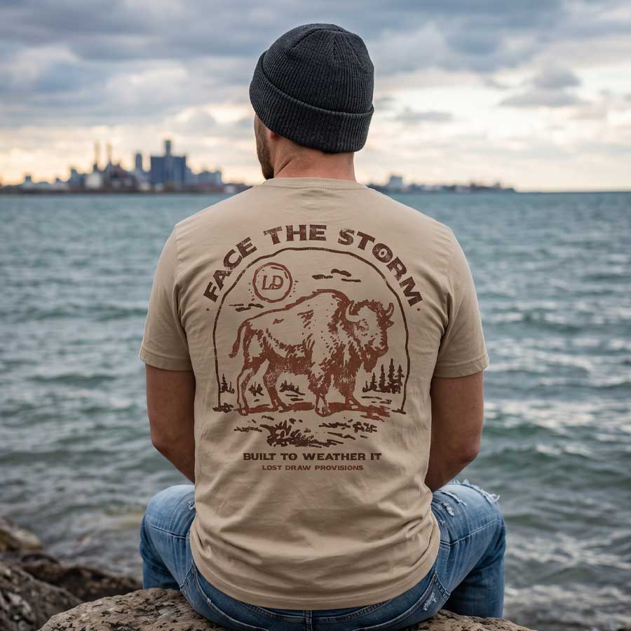 Man wearing the Face the Storm buffalo graphic tee beside a Great Lakes waterfront under cloudy skies.