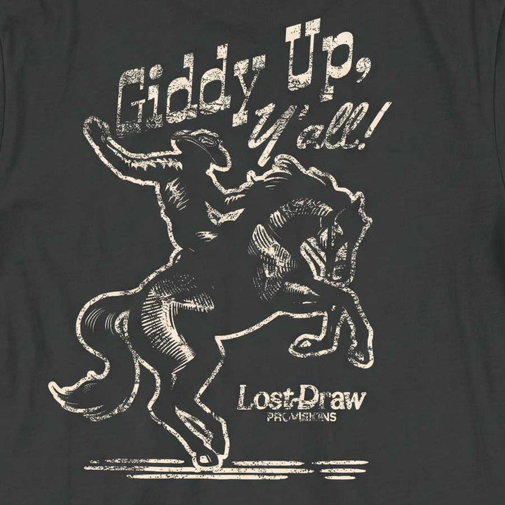 A close-up of a dark charcoal gray t-shirt featuring a distressed white graphic print of a cowboy riding a bucking horse, with the text &