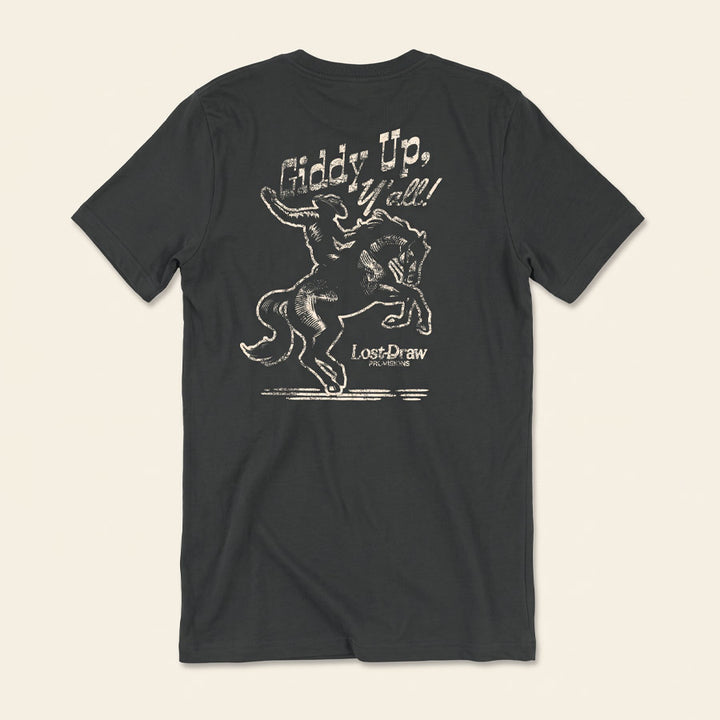 A dark charcoal gray t-shirt shown from the back, featuring a distressed white graphic of a cowboy riding a bucking horse with the text &