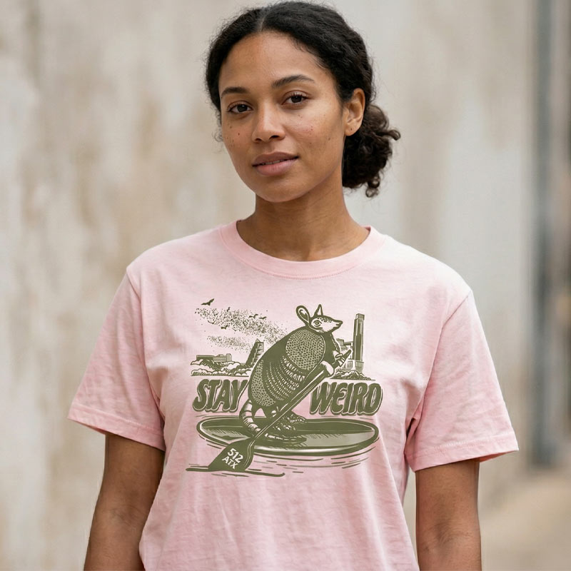 Woman wearing soft pink Stay Weird 512 boxy t-shirt with armadillo and Austin skyline graphic