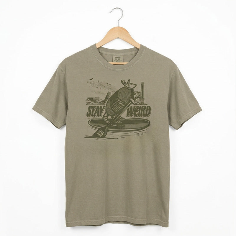 Austin skyline shirt with armadillo on paddleboard stay weird graphic on a hanger against a white background