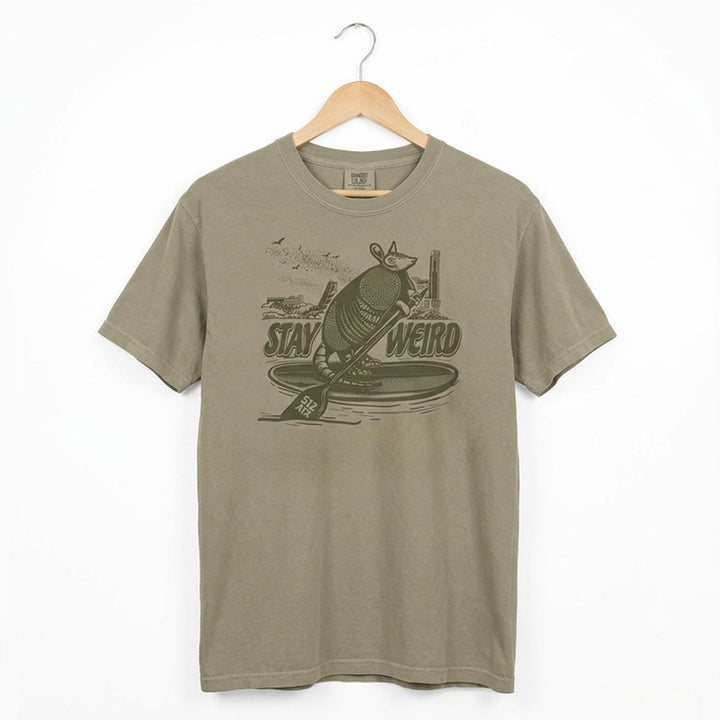 Austin skyline shirt with armadillo on paddleboard stay weird graphic on a hanger against a white background
