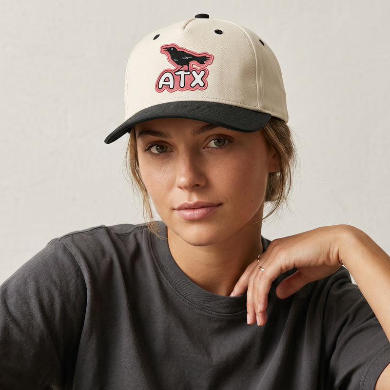 Studio shot of a woman wearing ATX Perch structured cotton twill hat with Austin-inspired bird patch detail