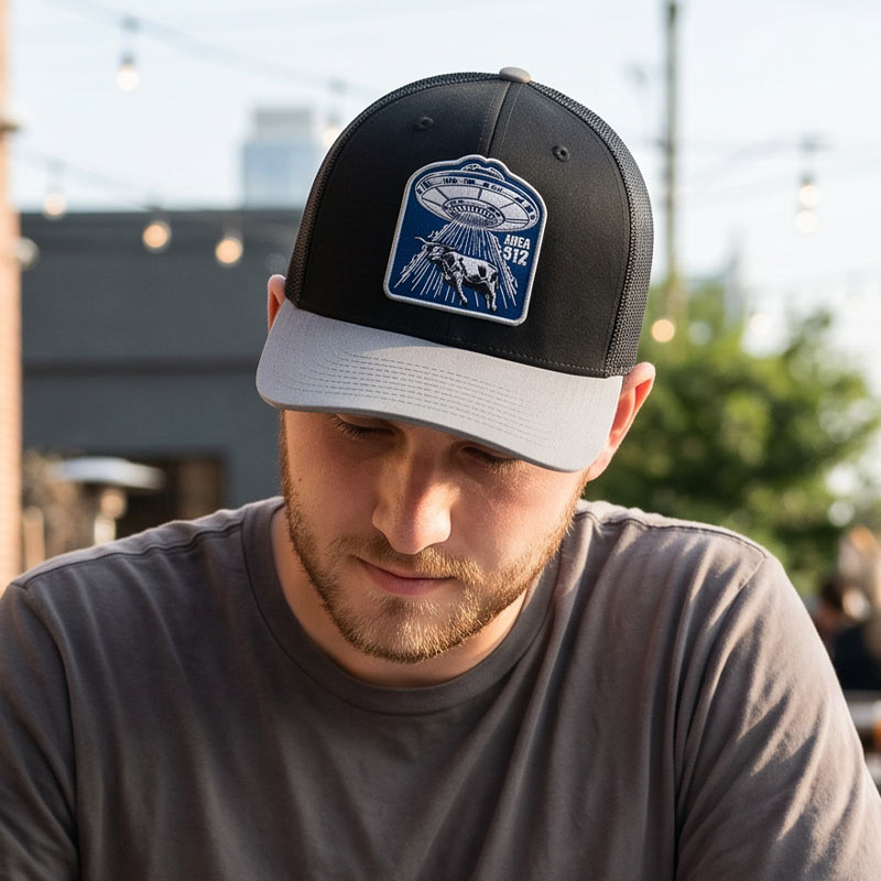 Person wearing the Area 512 trucker hat outdoors in natural light, showing the UFO longhorn patch on a black and light grey Richardson snapback cap.