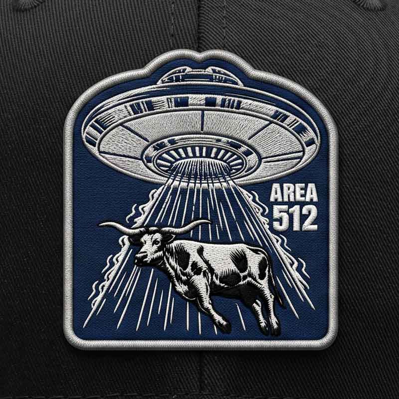 Close-up detail of the Area 512 UFO patch featuring a flying saucer, longhorn graphic, and embroidered-look texture on a black trucker hat.