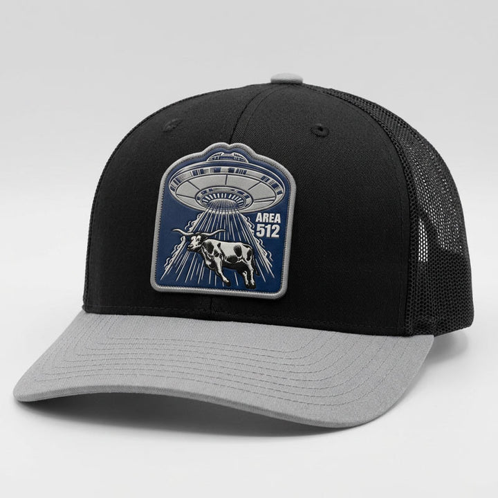 Black and light grey Richardson 112 snapback trucker hat featuring an Area 512 UFO patch with a flying saucer beaming up a Texas longhorn. Structured black front, breathable mesh back, and curved light grey bill.