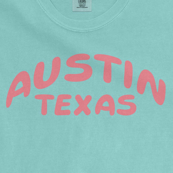 close up view of a Chalky Mint Comfort Colors 1717 heavyweight unisex t-shirt featuring a coral Austin Texas graphic across the chest.