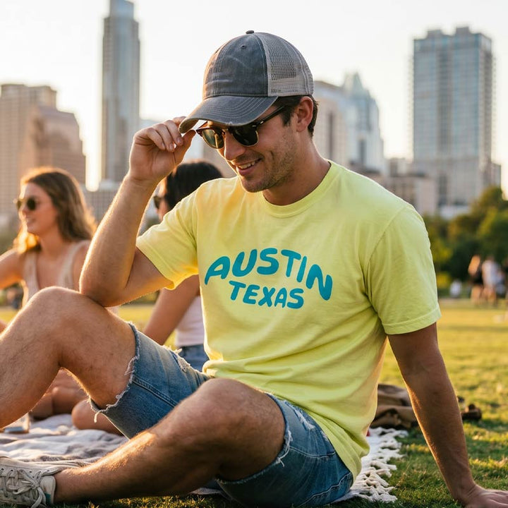 Man wearing a Neon Lemon Comfort Colors 1717 Austin t-shirt with aqua blue graphic at Zilker Park with the Austin skyline in the background.