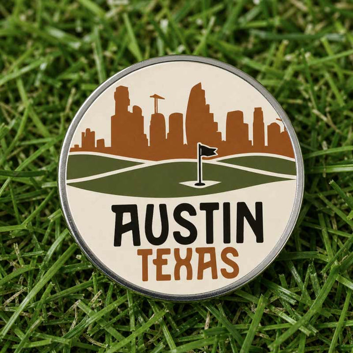 A round Austin Texas golf pin or badge featuring a brown city skyline, green golf course landscape with a hole flag, and &