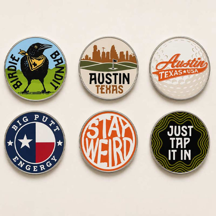 Six round golf-themed enamel pins arranged in a 2x3 grid on a light beige background. The pins feature designs including a bird with a bandana, an Austin Texas skyline, an Austin Texas USA golf ball texture, Big Putt Engergy with a Texas flag, &