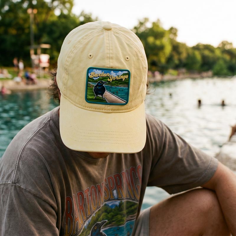 Person wearing Barton Springs hat outdoors in Austin Texas near water