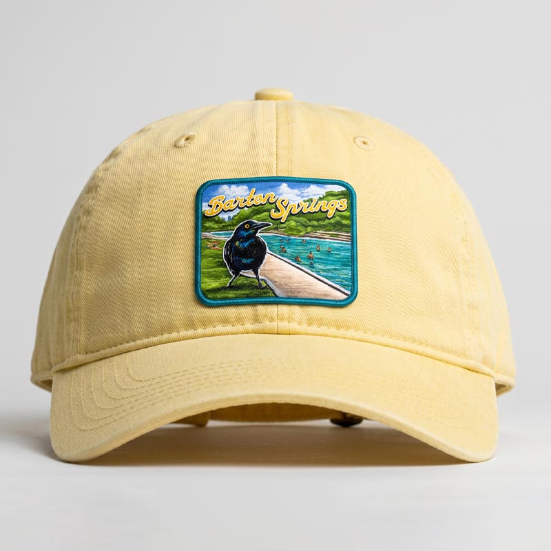 Butter-colored Barton Springs hat with UV printed patch featuring Austin grackle and Barton Springs pool scene