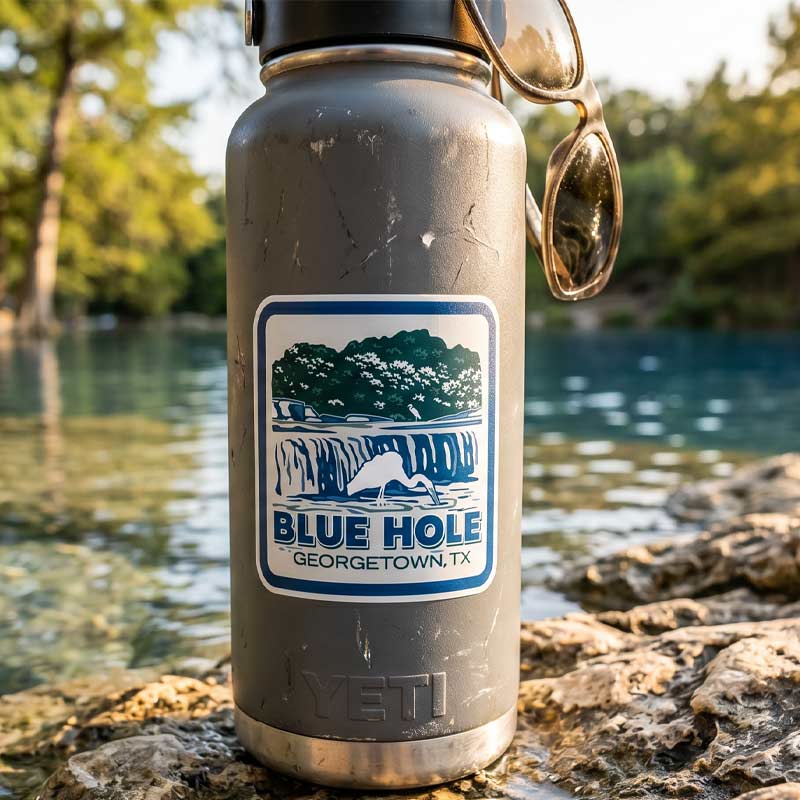 Silver Yeti water bottle with Blue Hole Georgetown, TX label on a rock by a river