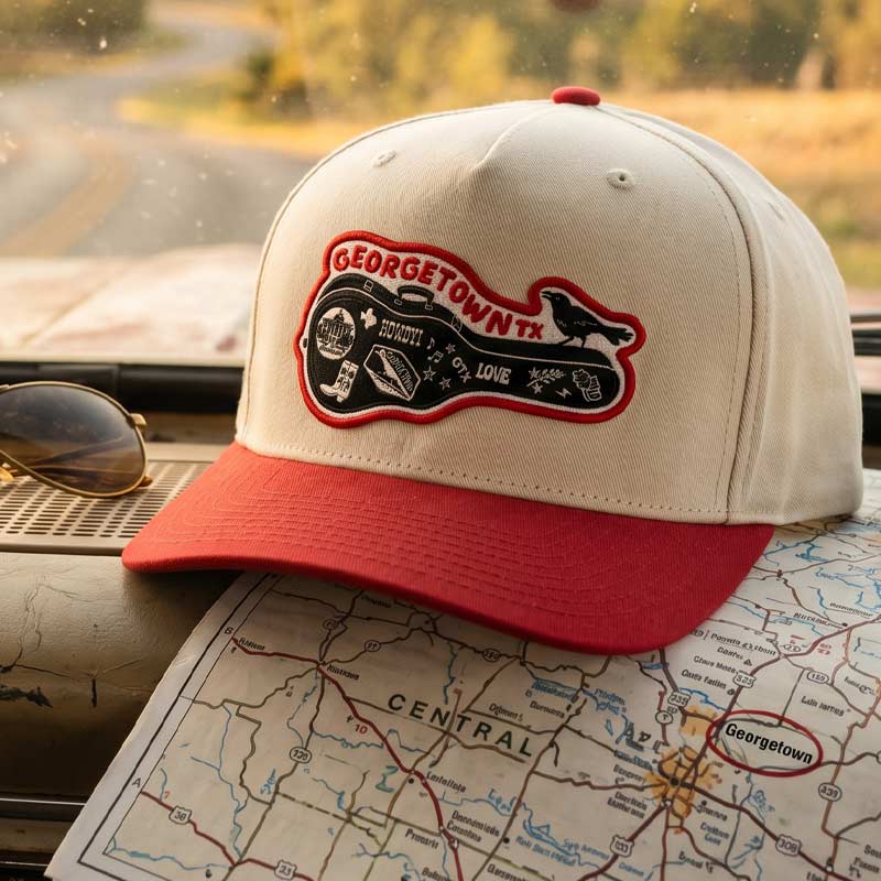 Carry-On Georgetown Hat resting on a Texas road map inside a vehicle, featuring the Georgetown guitar-case patch in warm golden-hour light.