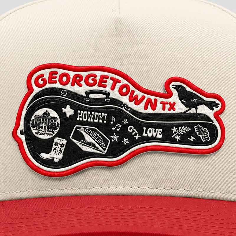 Close-up front view of the Carry-On Georgetown Hat highlighting the Georgetown guitar-case patch, grackle artwork, and cream/red five-panel construction.