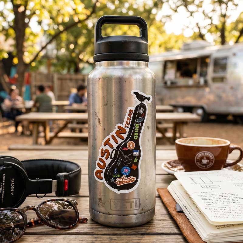 Silver YETI bottle with stickers on a wooden table outdoors, with people and a food truck in the background.