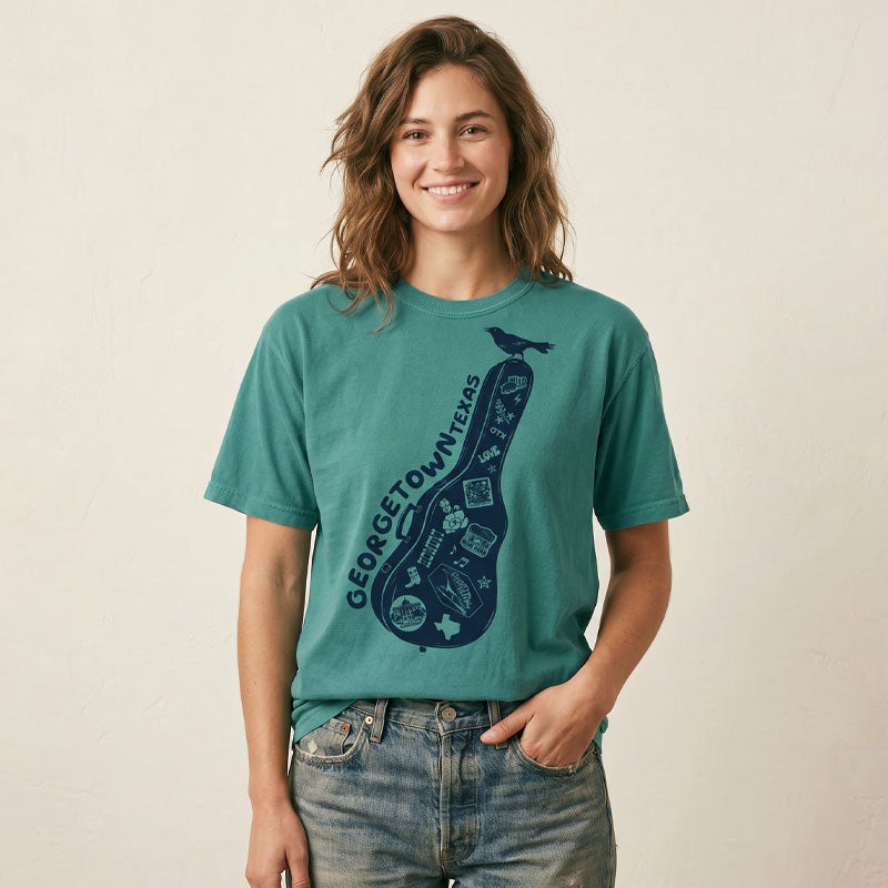 Woman wearing Carry-On Georgetown Texas T-shirt on seafoam Comfort Colors tee with guitar case graphic and local Georgetown icons