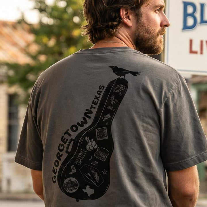 Man wearing Carry-On Georgetown oversized boxy tee in charcoal oil wash near a Texas music venue featuring oversized Georgetown guitar case back graphic.