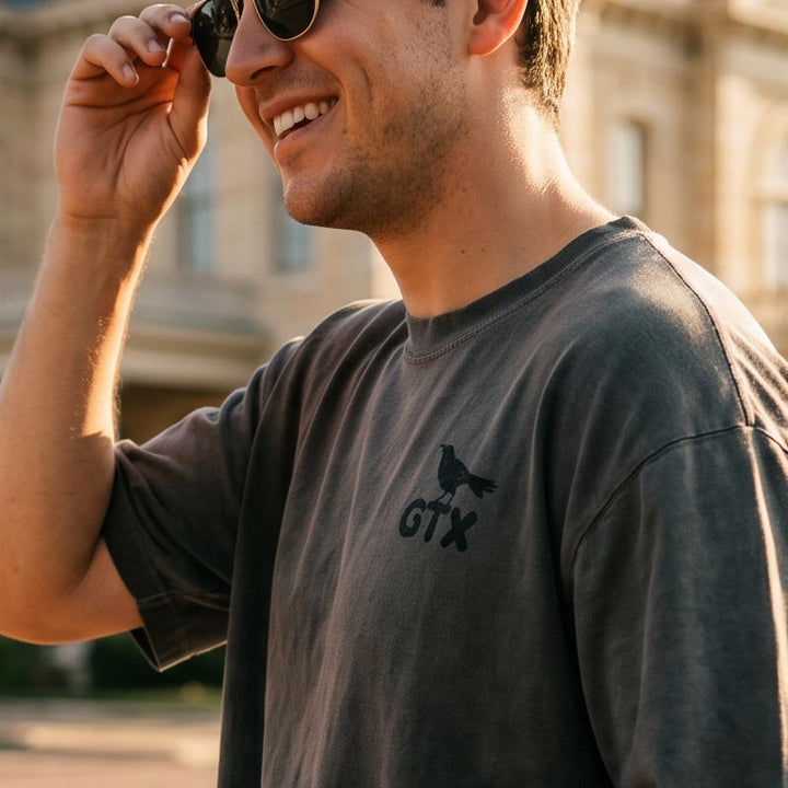 Man walking through downtown Georgetown Texas wearing the Carry-On Georgetown oversized boxy tee in charcoal oil wash with small GTX grackle chest graphic.