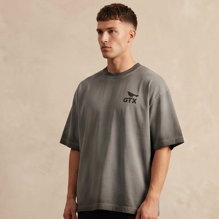 Model wearing Carry-On Georgetown oversized boxy tee in charcoal oil wash with relaxed heavyweight fit and GTX grackle graphic.