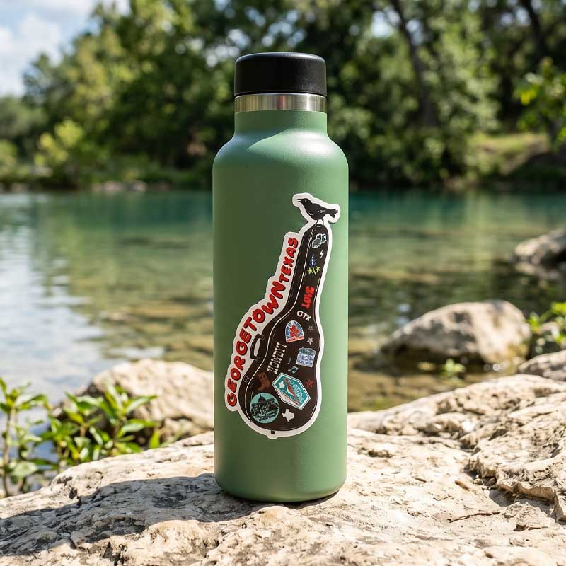 Green water bottle with stickers on a rock by a river