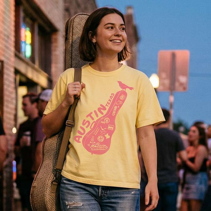 Lifestyle image of woman wearing relaxed fit Austin music graphic tee, holding a guitar case in an urban setting.