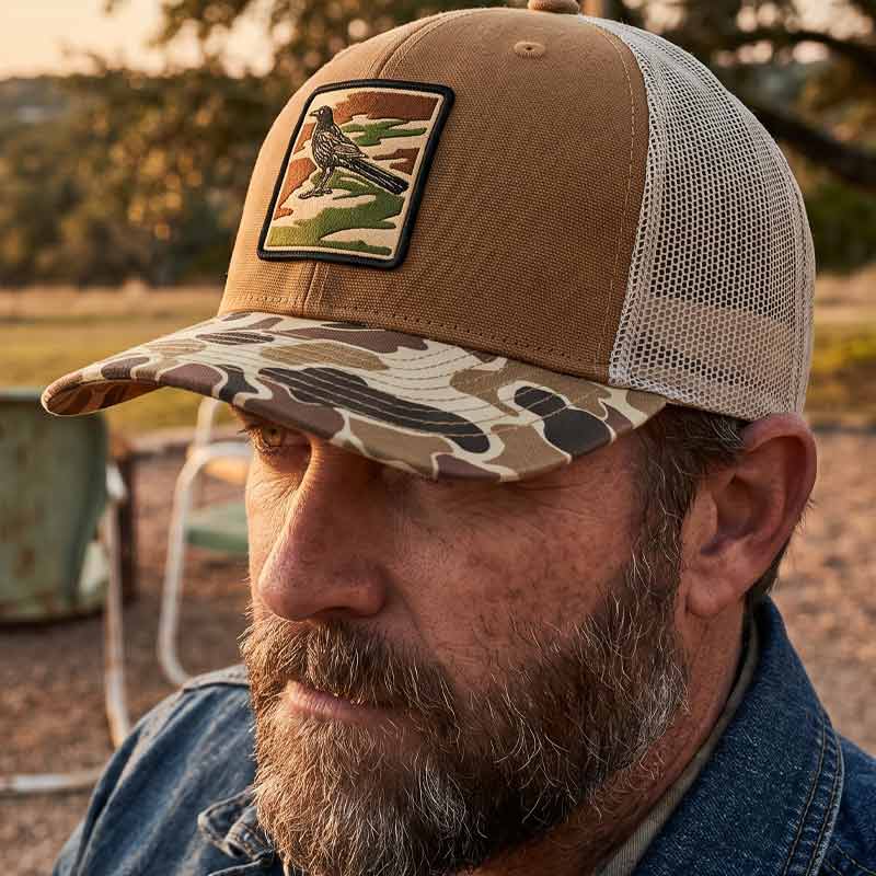Bearded man wearing Saddle and duck camo DRI DUCK trucker hat with UV printed grackle camouflage patch designed to look embroidered