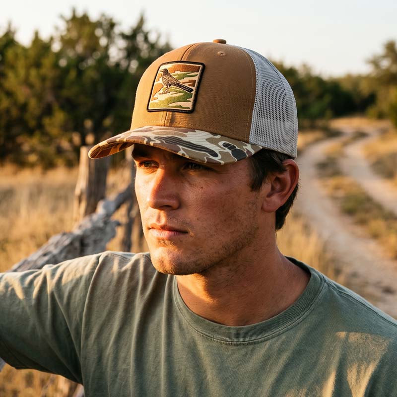 Man wearing Saddle and duck camo DRI DUCK trucker hat with UV printed grackle camouflage patch designed to look embroidered