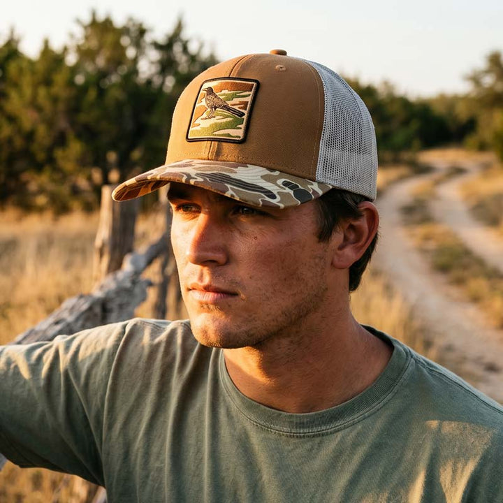 Man wearing Saddle and duck camo DRI DUCK trucker hat with UV printed grackle camouflage patch designed to look embroidered