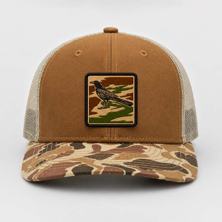 Product shot of Saddle and duck camo DRI DUCK trucker hat with UV printed grackle camouflage patch designed to look embroidered