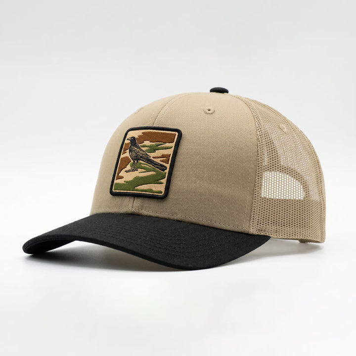 Angled view of the City Camo Grackle Richardson 112 trucker hat in khaki and black showing the curved brim, mesh back, and detailed grackle camo patch.