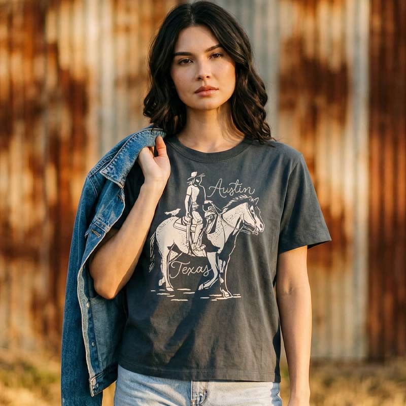 Woman wearing washed black Dust & Reins Austin boxy t-shirt with western rider graphic