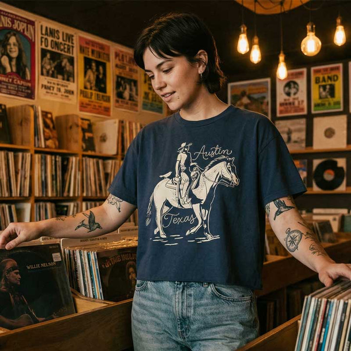 Woman wearing washed black Dust & Reins Austin boxy t-shirt with western rider graphic in a record store.