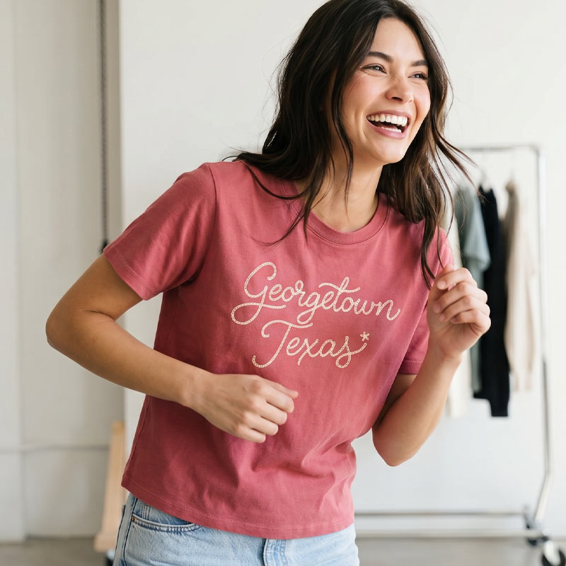 Woman wearing a Georgetown Texas women’s boxy t-shirt in garment-dyed red with vintage chainstitch-style script graphic and relaxed cropped fit