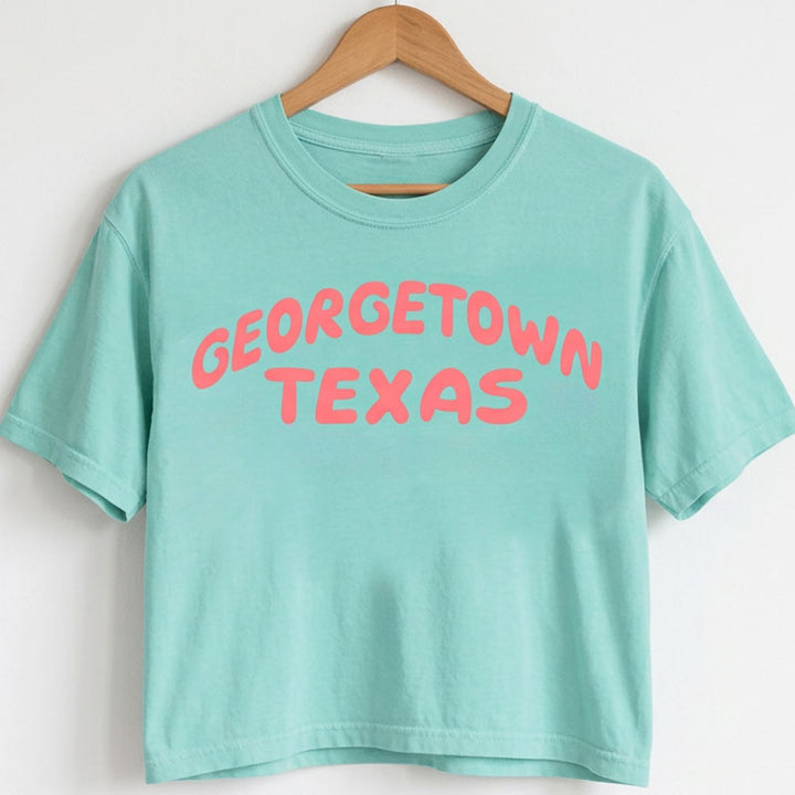Georgetown Texas women’s boxy t-shirt in Chalky Mint with coral pop graphic on a wooden hanger against a white background