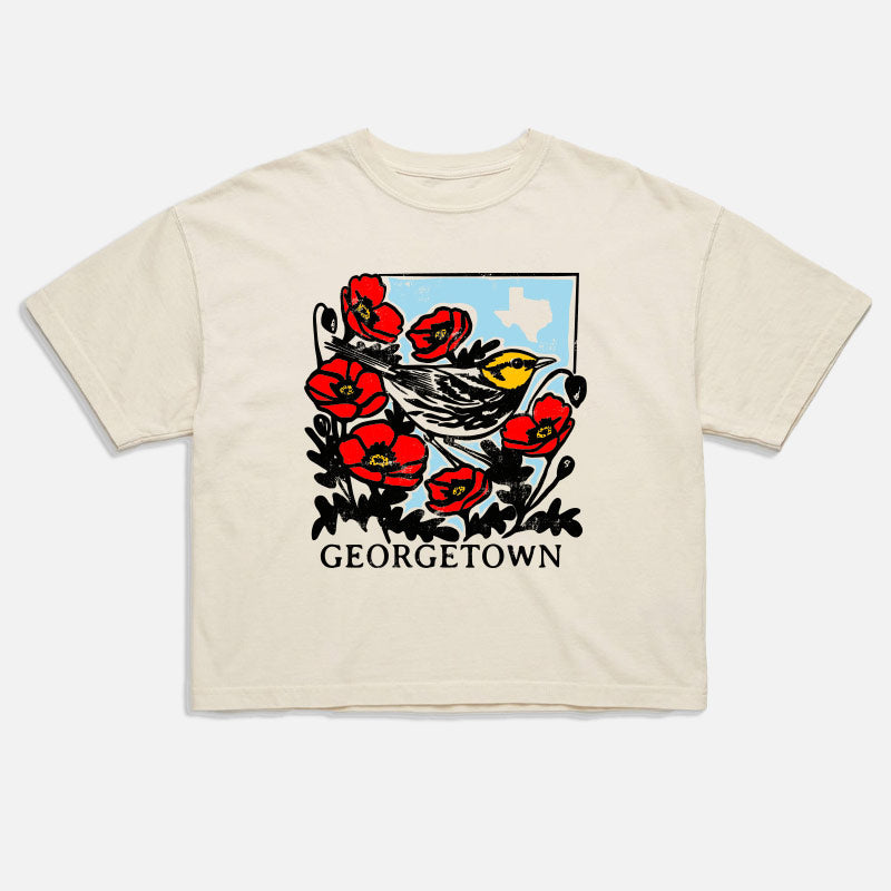 Flat lay of Georgetown Warbler women's boxy t-shirt with bird and poppy design on sky blue background