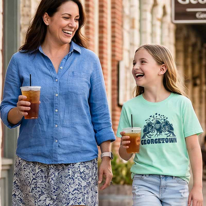 Young girl wearing Georgetown Grackle Gang mint youth tee with navy grackle graphic while walking with her mom in Georgetown, Texas.