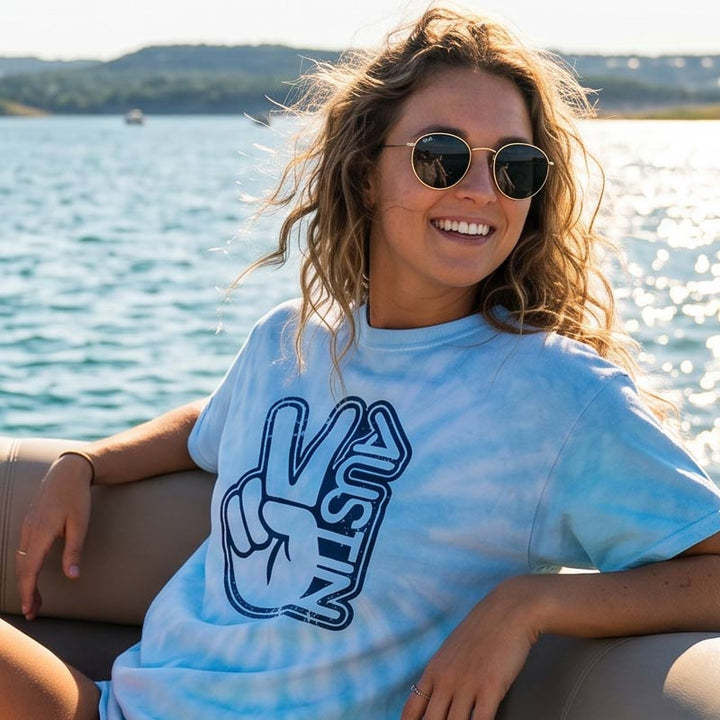 Woman wearing the Groovy Austin Blue Lagoon tie-dye t-shirt featuring a retro Austin peace sign graphic while enjoying a sunny day in Austin, Texas.