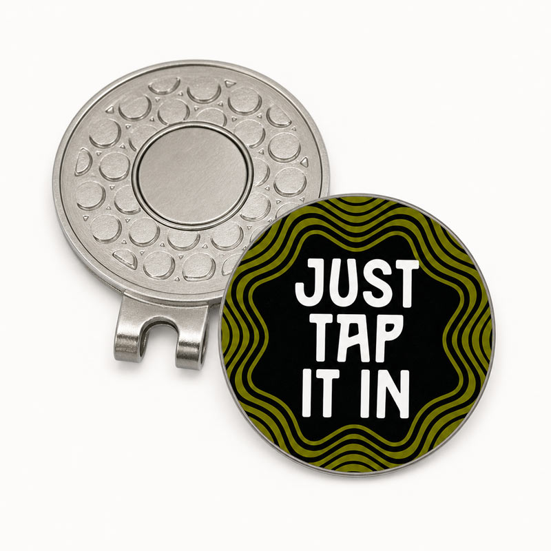 A round golf flag divot stake shown from both sides on a white background. One side is metallic silver with a textured pattern, and the other side is black with olive green wavy lines and the text &