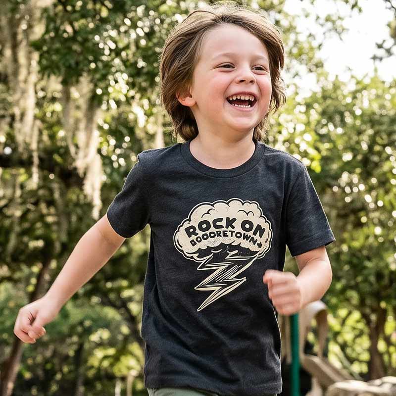 Kid wearing the dark grey Rock On Georgetown Georgetown TX youth t-shirt outdoors at a park in natural Texas sunlight.