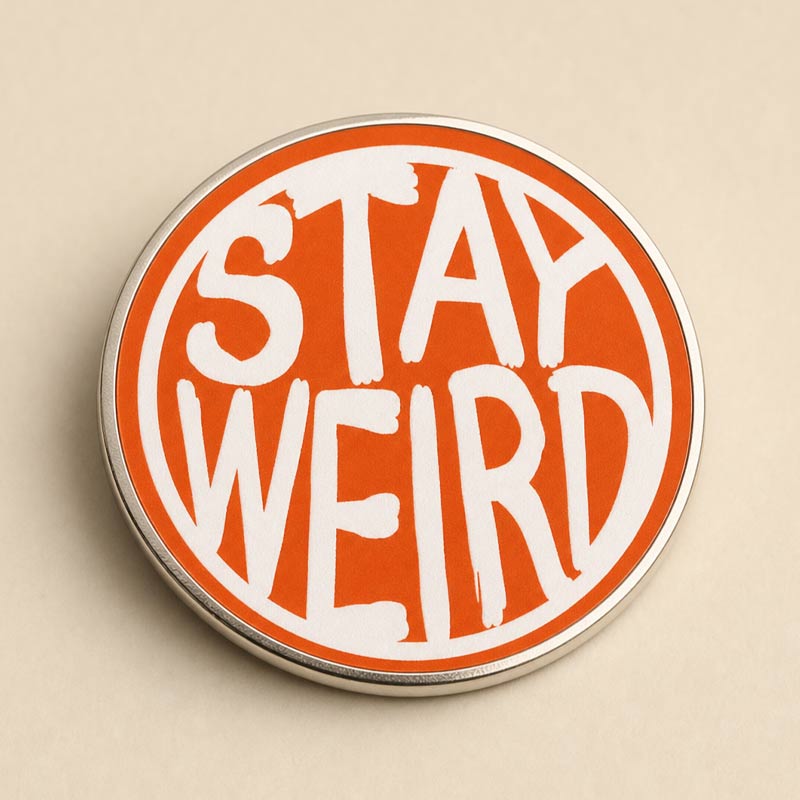 A circular enamel pin with a silver metal border, featuring a vibrant orange background and bold white hand-painted style text that reads &