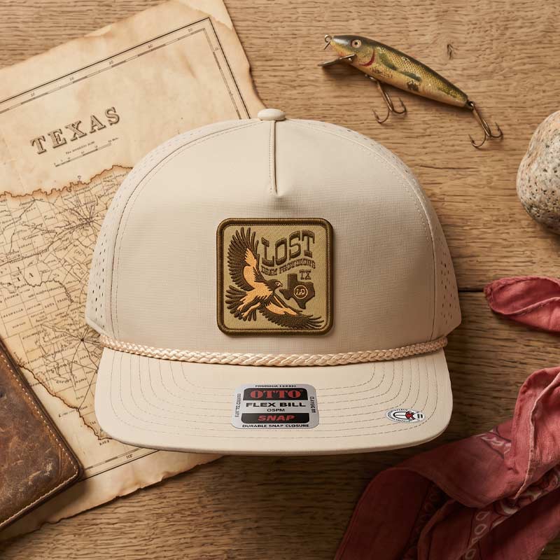 Beige cap with eagle logo on a wooden surface with fishing lure and map