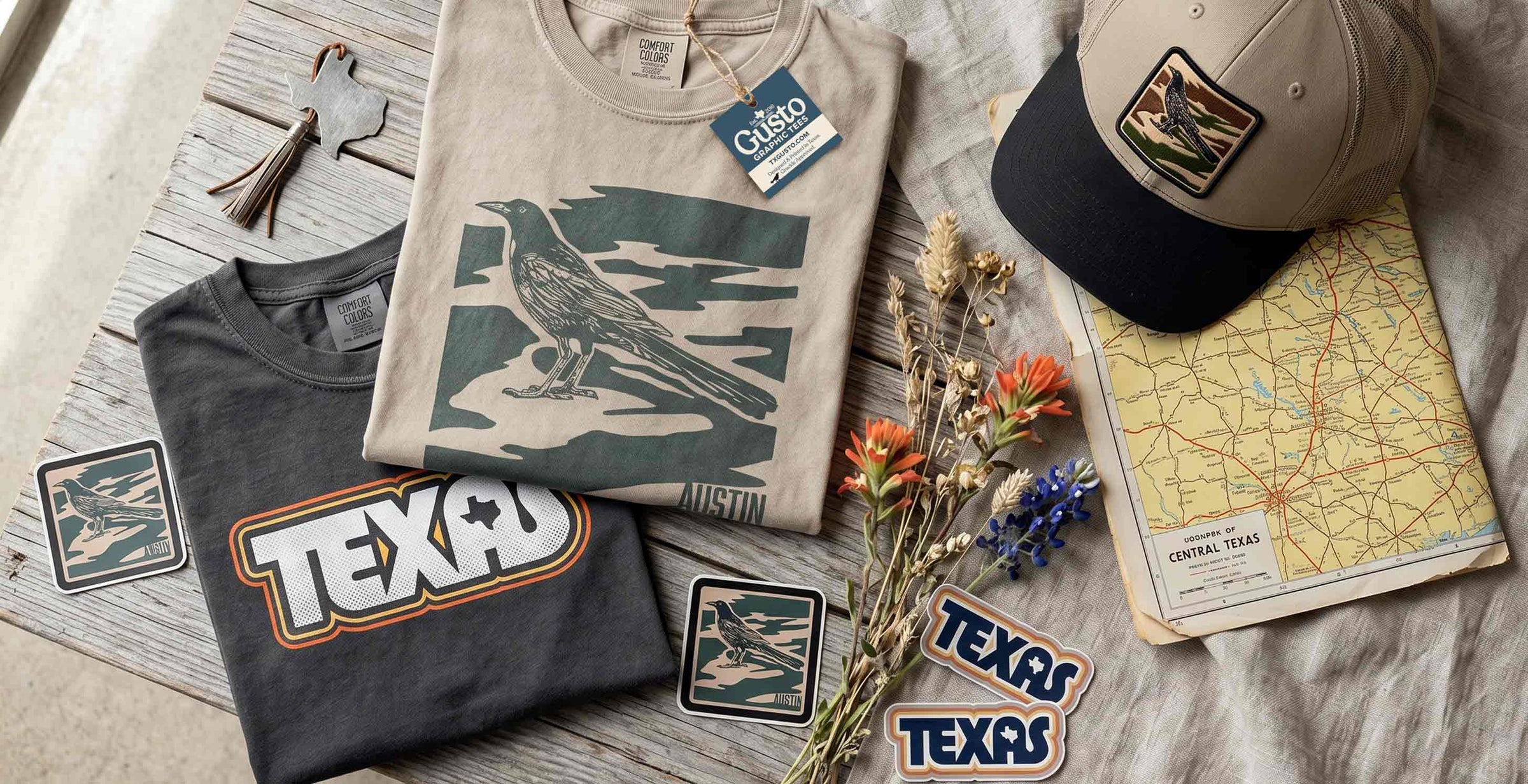 Collection of Texas-themed clothing and accessories on a wooden surface with a map and flowers.