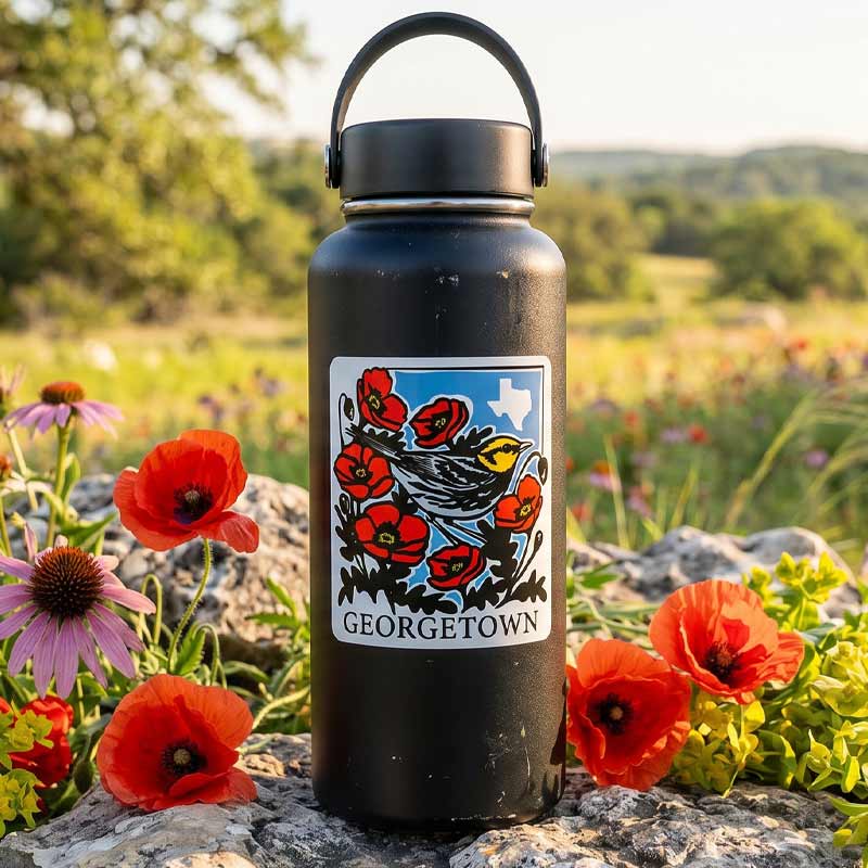Black water bottle with a colorful label featuring flowers and the word 'Georgetown' in a natural setting with flowers and rocks.
