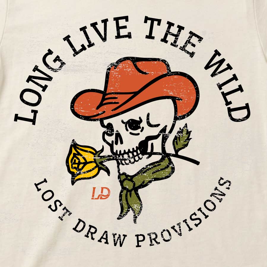Close-up of a cream-colored t-shirt featuring a distressed graphic of a cartoon skull wearing an orange cowboy hat and holding a yellow rose. The text &