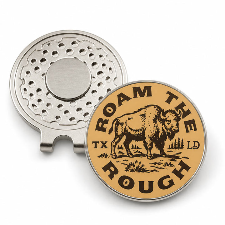 A silver metal golf divot holder shown from two angles: one side displaying the magnetic clip mechanism, and the other showing a round tan face with a black engraved bison and the text &