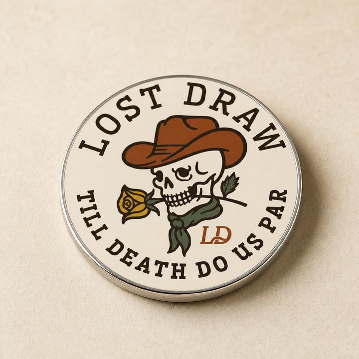 A round enamel pin featuring a skull wearing a brown cowboy hat and holding a yellow rose, with the text &
