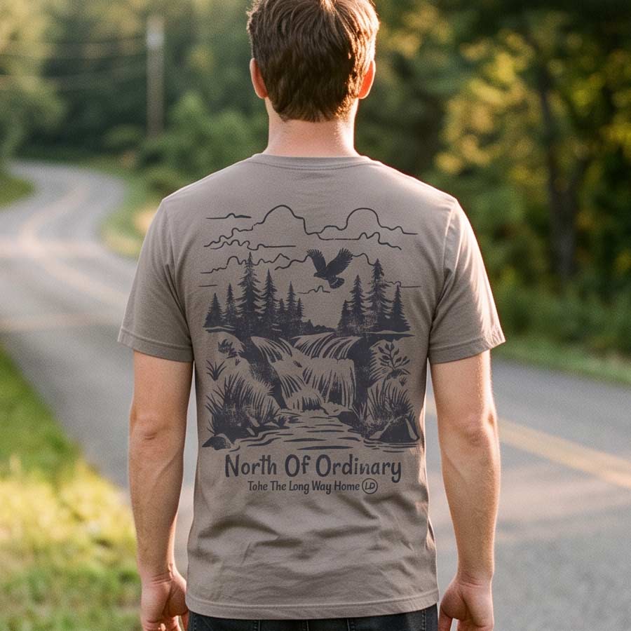 Man wearing the North of Ordinary Jersey Tee beside a tree-lined country road, displaying the waterfall and forest back graphic.