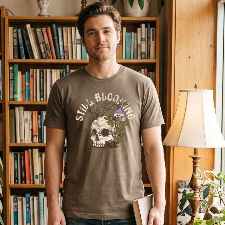 Man wearing the Vintage Brown Still Blooming Jersey Tee inside a bookstore, showing the skull and mushroom artwork.